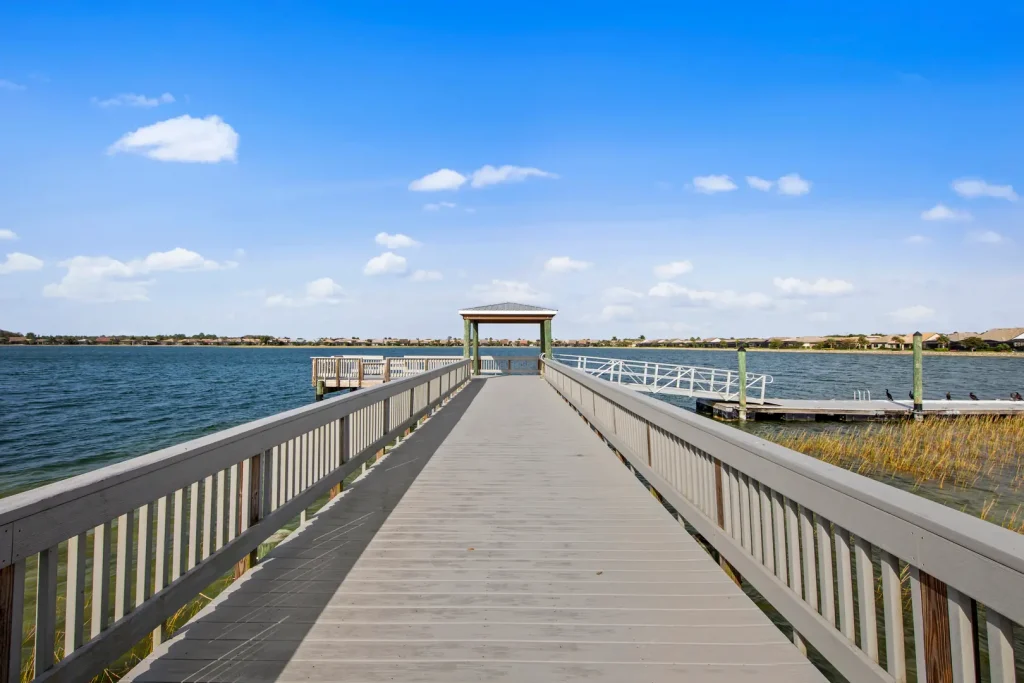 Wooden boardwalk extending toward a small gazebo over calm blue water, under a clear sky.