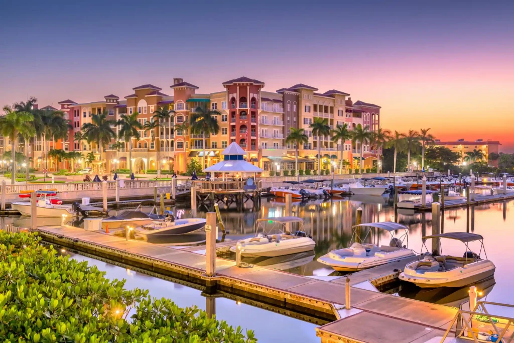 Colorful resort buildings along a marina at sunset with palm trees and moored boats.